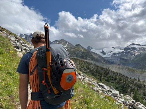 Wanderer mit Rucksack auf einem Bergweg, im Hintergrund schneebedeckte Berge.