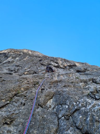 Ein Kletterer an einer steilen Felswand, Seil läuft nach oben zu ihm.