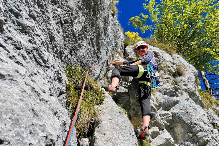 Frau klettert an einer Felswand, trägt Helm und Kletterausrüstung.