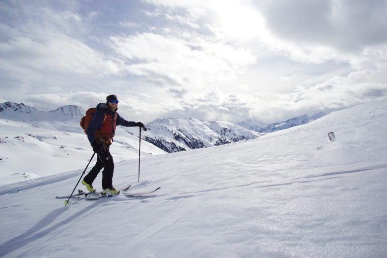 Skifahrer auf verschneitem Berg mit Gipfeln im Hintergrund.