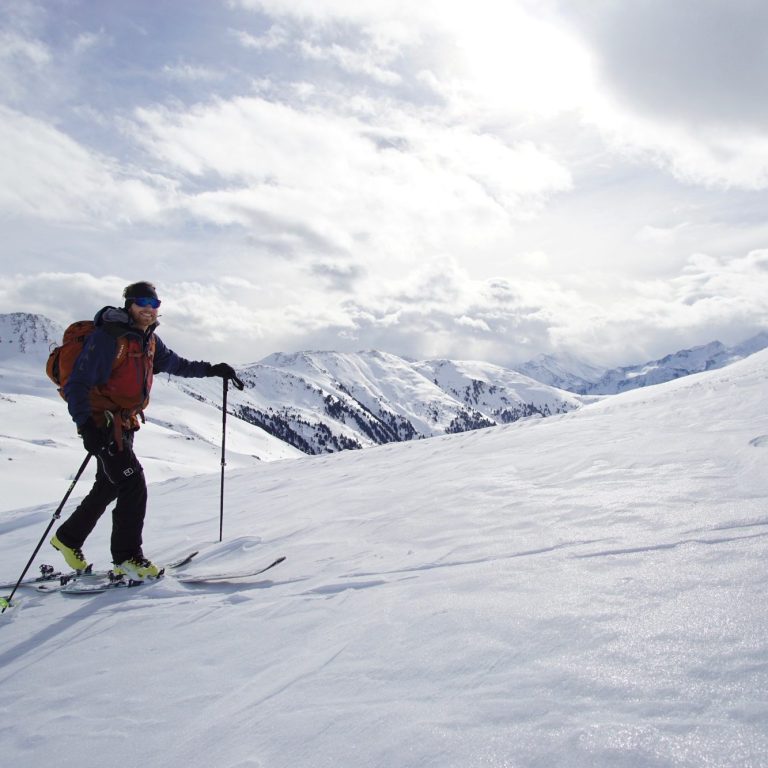 Skifahrer auf einer verschneiten Berglandschaft unter bewölktem Himmel.