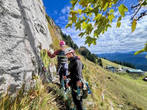 Zwei Kletterer am Fels im Freien, umgeben von Landschaft und Bäumen.