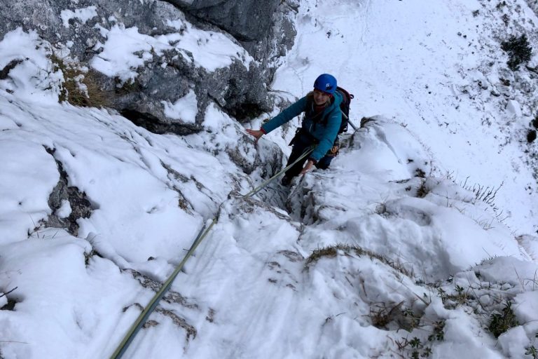 Ein Kletterer erklimmt einen gefrorenen Hang in einer schneebedeckten Landschaft.