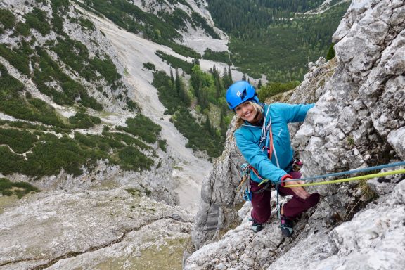Person in blauer Kletterausrüstung, die eine Felswand in den Bergen erklimmt.