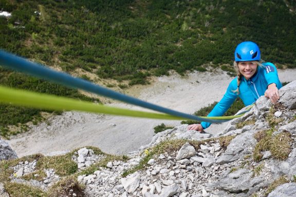 Eine kletternde Person sichert sich mit Seilen an einer Felswand in der Natur.