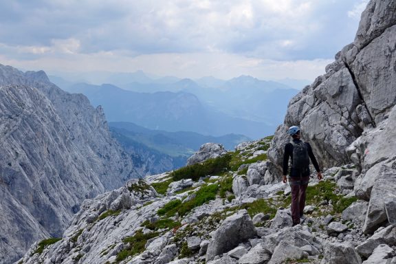 Wanderer auf einem felsigen Bergpfad mit Blick auf eine malerische Berglandschaft.
