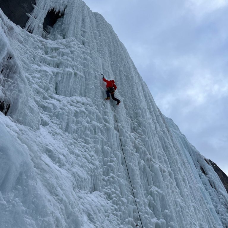 Ein Kletterer in roter Jacke erklimmt eine gefrorene Wasserfallwand.