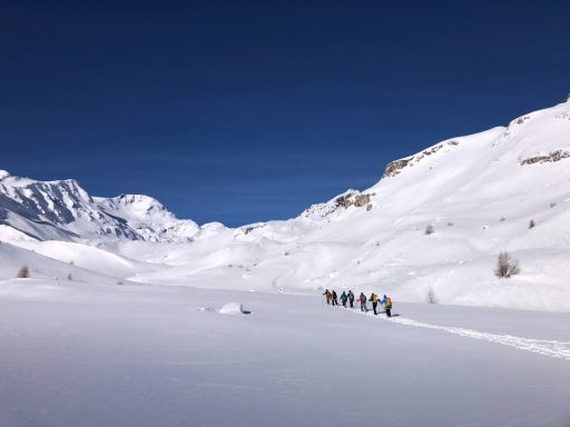 Wanderer durch eine schneebedeckte Landschaft unter blauem Himmel.