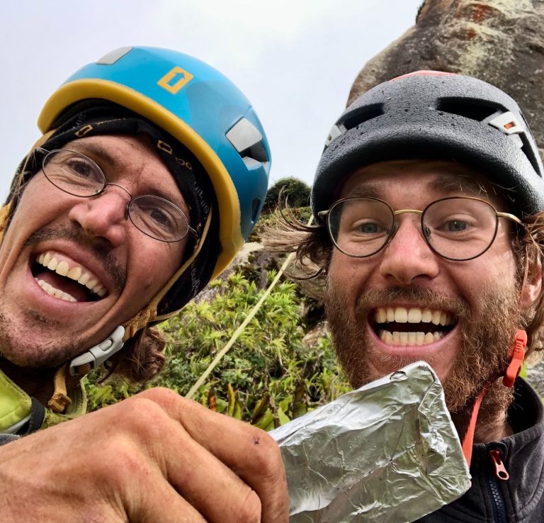 Zwei fröhliche Bergsteiger posieren mit Kletterausrüstung in der Natur.