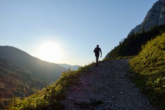 Wanderer auf einem Pfad in der Berglandschaft bei Sonnenuntergang.