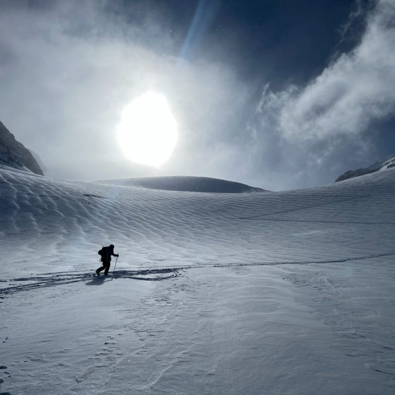 Ein Skitourengeher bewegt sich durch verschneite Landschaft bei sonnigem Wetter.