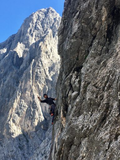 Kletterer an einer steilen Felswand mit Bergen im Hintergrund.