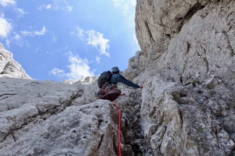 Ein Kletterer, der eine steile Felswand erklimmt, gesichert mit einem Seil.