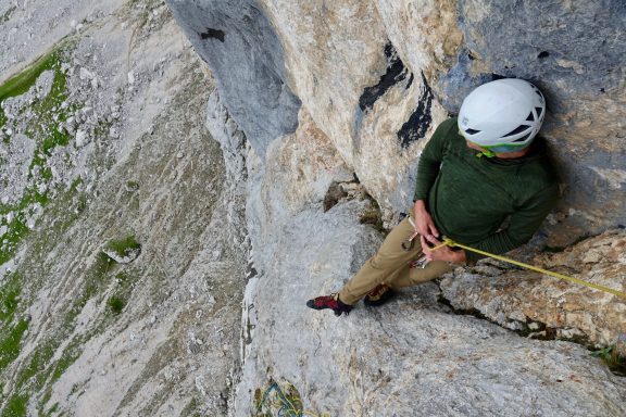 Ein Kletterer sitzt an einer Felswand und sichert sich mit einem Seil.
