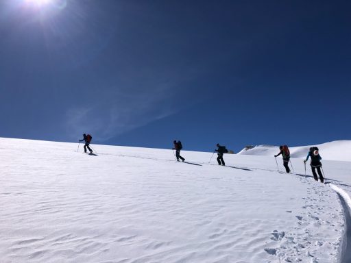 Fünf Personen besteigen eine verschneite Berglandschaft bei klarem Himmel.