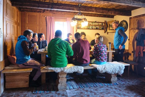 Skitouren Camp Rofan Gruppe von Menschen an einem Tisch in einer gemütlichen Hütte beim Essen und Reden.