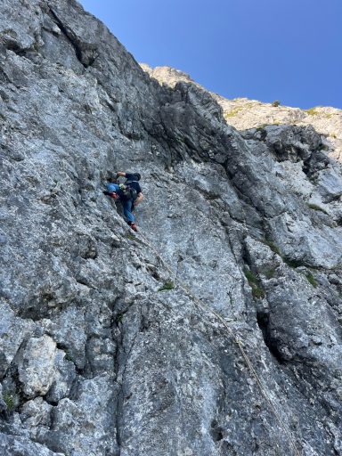 Kletterer an einer steilen Felswand unter klarem Himmel.