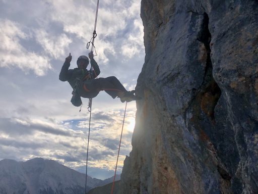 Kletterer schwingt an einem Seil vor einer felsigen Wand bei Sonnenuntergang.