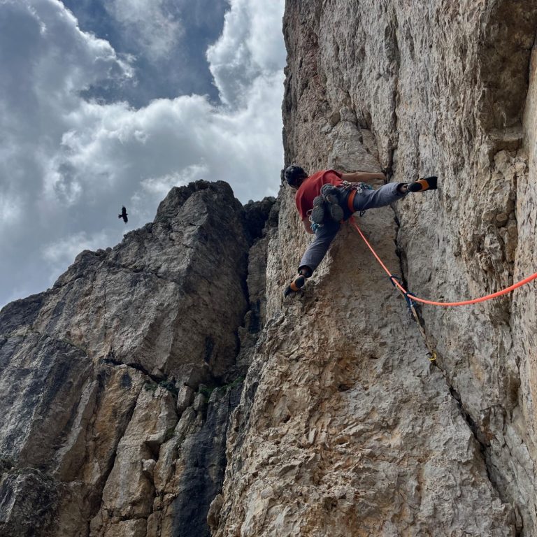 Kletterer an einer steilen Felswand mit Seil, Wolken im Hintergrund.