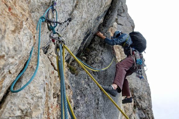 Eine Person klettert an einer Felswand mit Sicherungsseilen.
