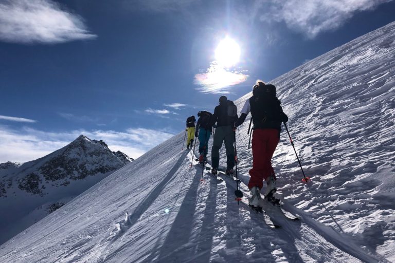Gruppe von Skifahrern auf einer schneebedeckten Berghang mit Sonnenschein.