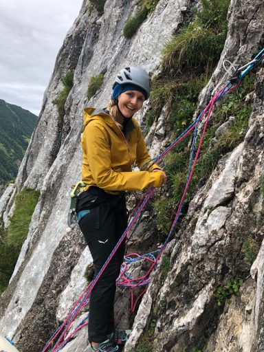Frau in gelber Jacke bei einer Kletterroute an einer Felswand.