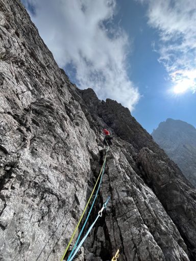 Kletterer erklimmt steile Felswand unter einem bewölkten Himmel.