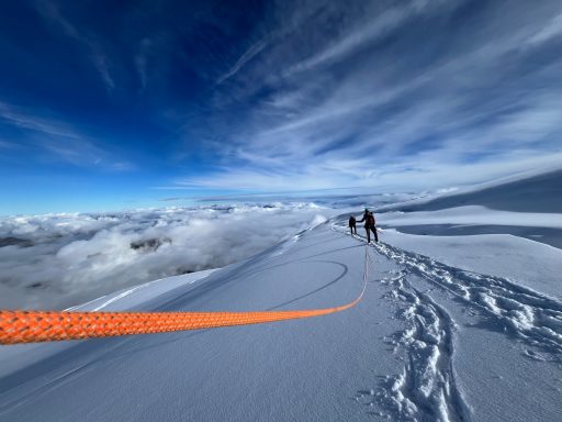 Personen gehen auf einem schneebedeckten Bergweg unter einem blauen Himmel.