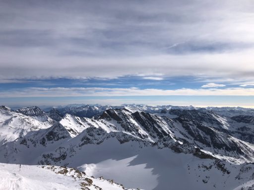 Weitreichende Berglandschaft mit schneebedeckten Gipfeln und bewölktem Himmel.
