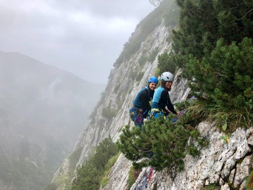 Zwei Kletterer an einer steilen Felswand in nebliger Umgebung.
