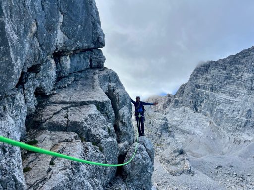 Kletterer auf einem schmalen Grat zwischen steilen Felsen mit grüner Kletterleine.