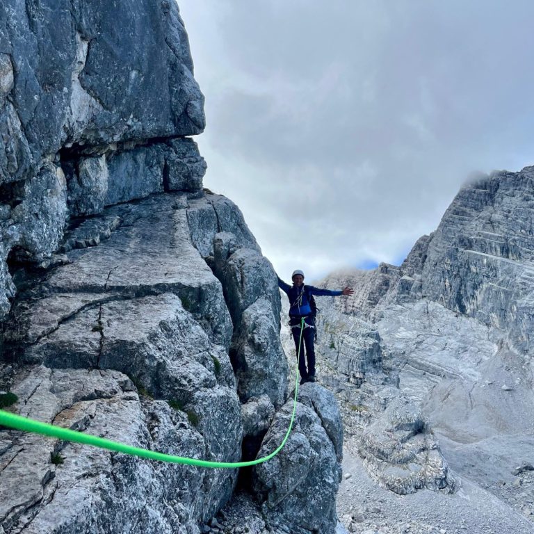 Person balanciert auf einem Seil zwischen Felsen in einer bergigen Landschaft.