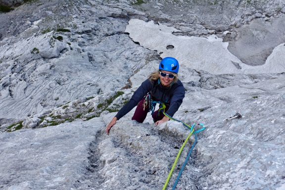 Kletterer in blauer Helmkappe, der eine Felswand mit Seil hochsteigt.