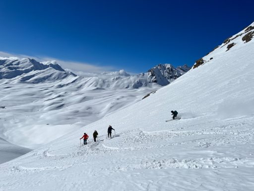Skifahrer gleiten über verschneite Berge unter klarem blauen Himmel.
