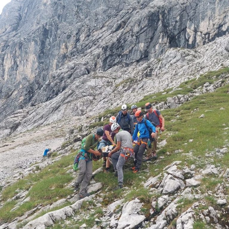 Kletterer an einer Felswand mit einem Seil, umgeben von Bergen und Wolken.