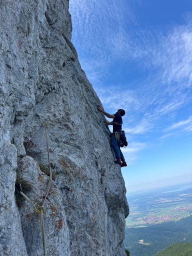 Person klettert an einer Felswand mit Blick auf die Landschaft.
