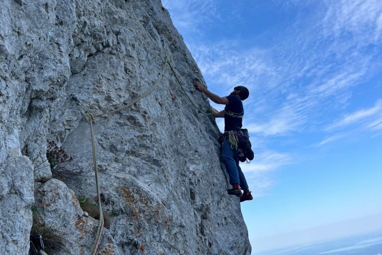 Frau in Helm klettert an einer Felswand und greift nach einem Griff.