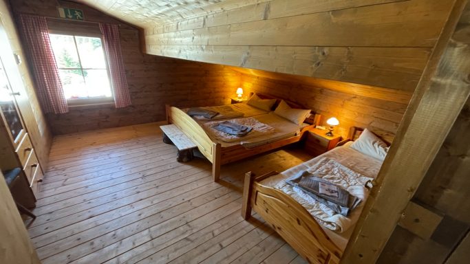Skitouren Camp Rofan Zwei Holzbetten in einem hellen, rustikalen Zimmer mit Fenster und warmem Licht.