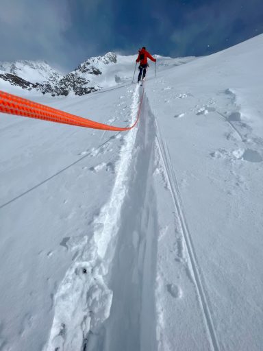 Ein Bergsteiger in rot steigt einen verschneiten Hang mit Steigeisen und Seil.