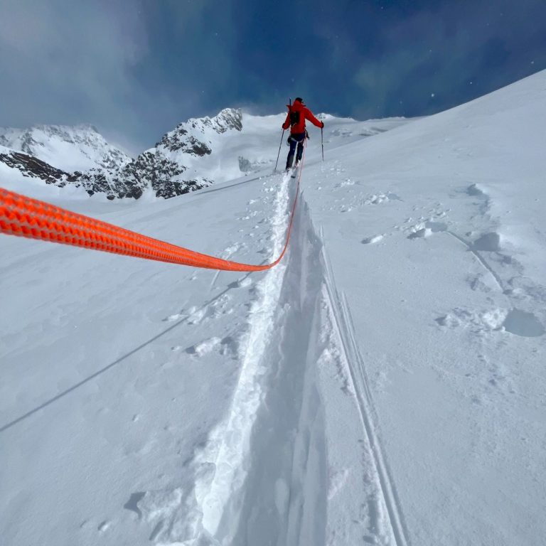 Eine Person steigt auf einem schneebedeckten Berg mit orangefarbenem Seil.