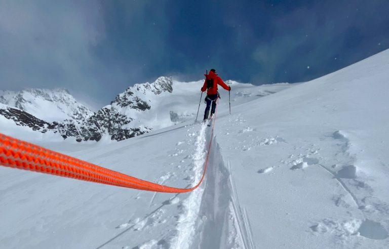 Skifahrer auf verschneiter Piste mit Berglandschaft und Sonne im Hintergrund.