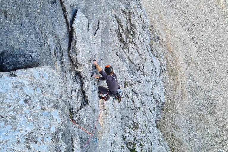 Kletterer, der eine steile Felswand erklimmt, gesichert durch Seil.