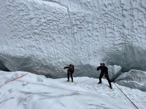Zwei Bergsteiger klimmen an einer Gletscherwand mit einer großen Eisfläche im Hintergrund.