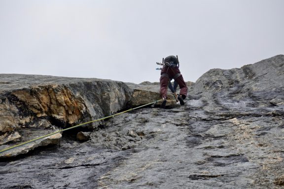 Alpinist klettert eine steile Felswand mit Ausrüstung und Seil.