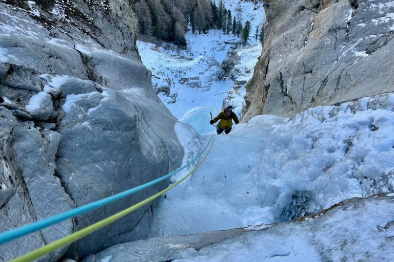 Kletterer, der in eine schneebedeckte Schlucht abseilt, umgeben von steilen Felsen.
