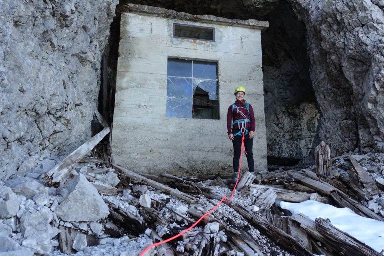 Bergsteiger steht vor einem verlassenen Gebäude in einer Felslandschaft.