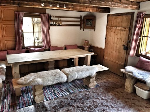 Skitouren Camp Rofan Gemütlicher Raum mit Holz-Tisch, Bänken, Teppich und Fenster mit Vorhängen.