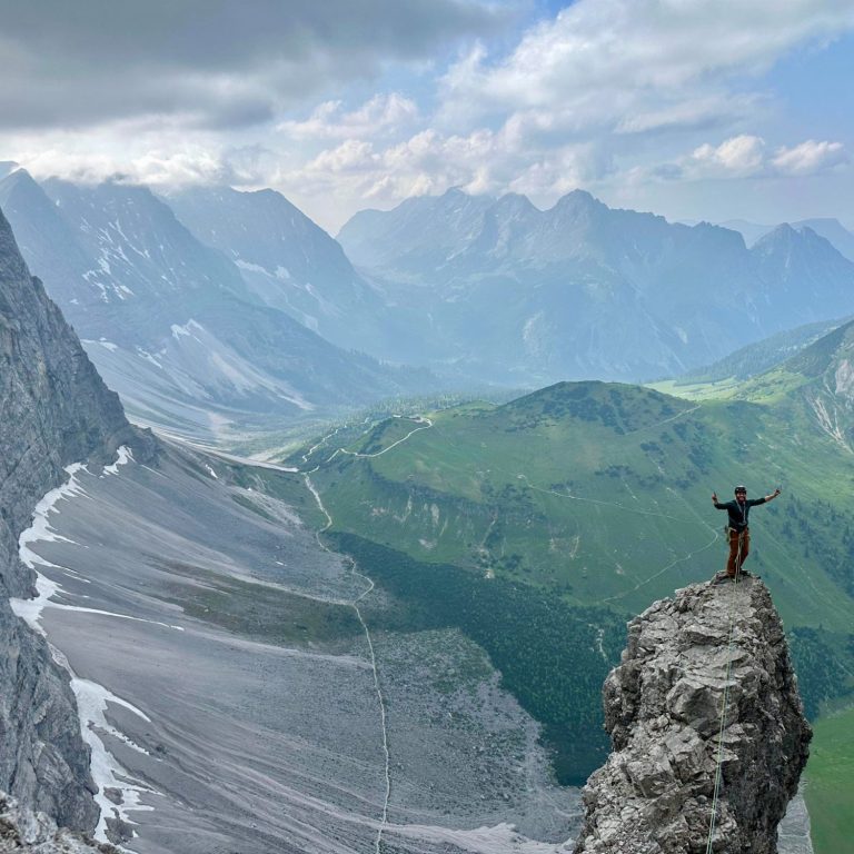 Person steht auf einem Felsen mit Blick auf eine beeindruckende Berglandschaft.