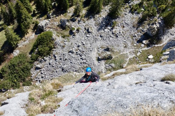 Ein Kletterer mit Helm, der einen Felsen hinaufklettert, umgeben von Natur.