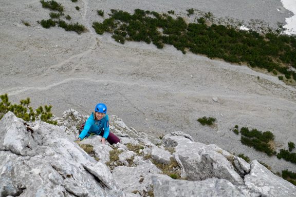 Eine Person klettert einen felsigen Hang in einer gebirgigen Landschaft.